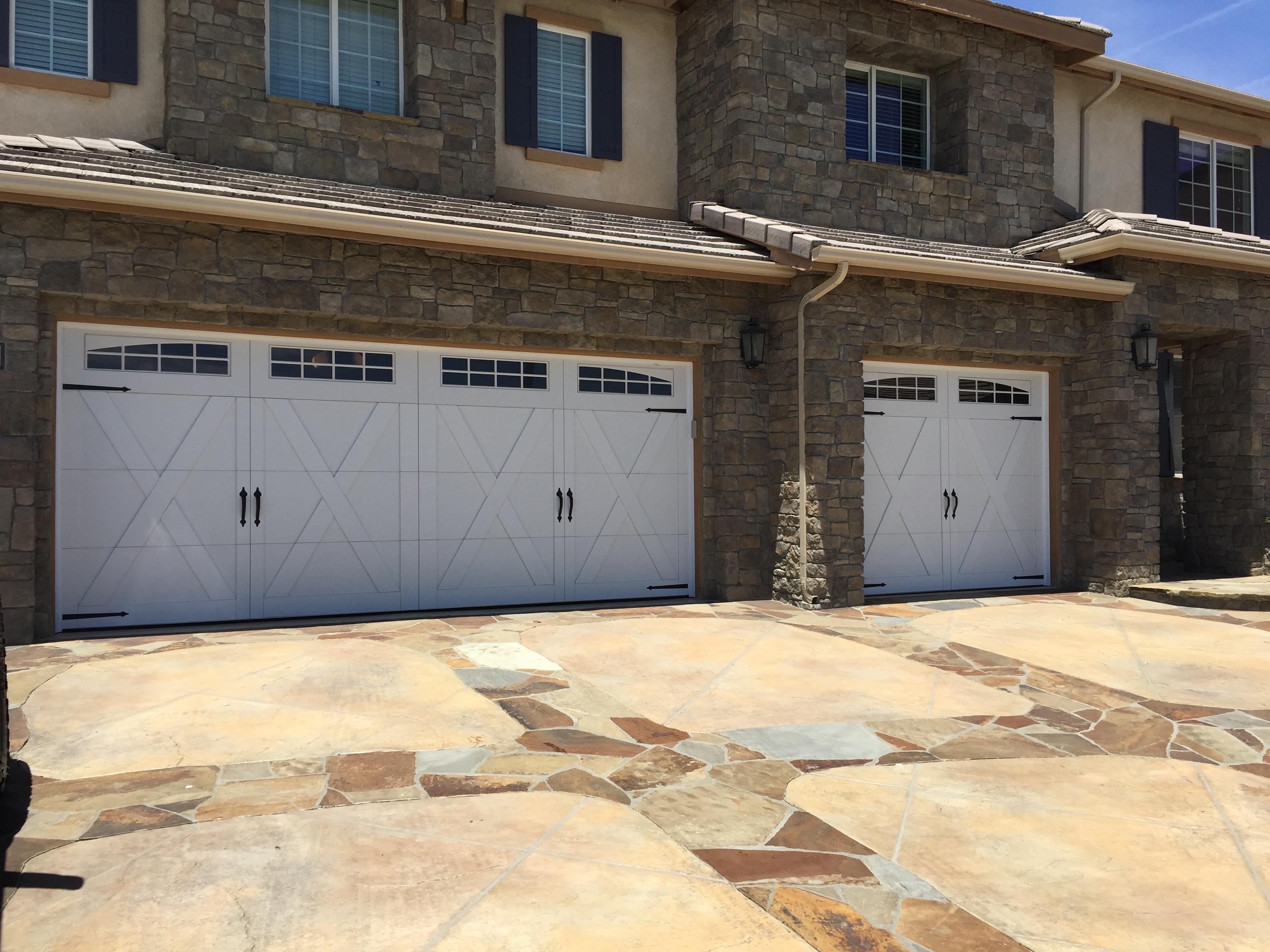 Triple white carriage-style garage doors with decorative iron hardware on a stone-clad Antelope Valley home